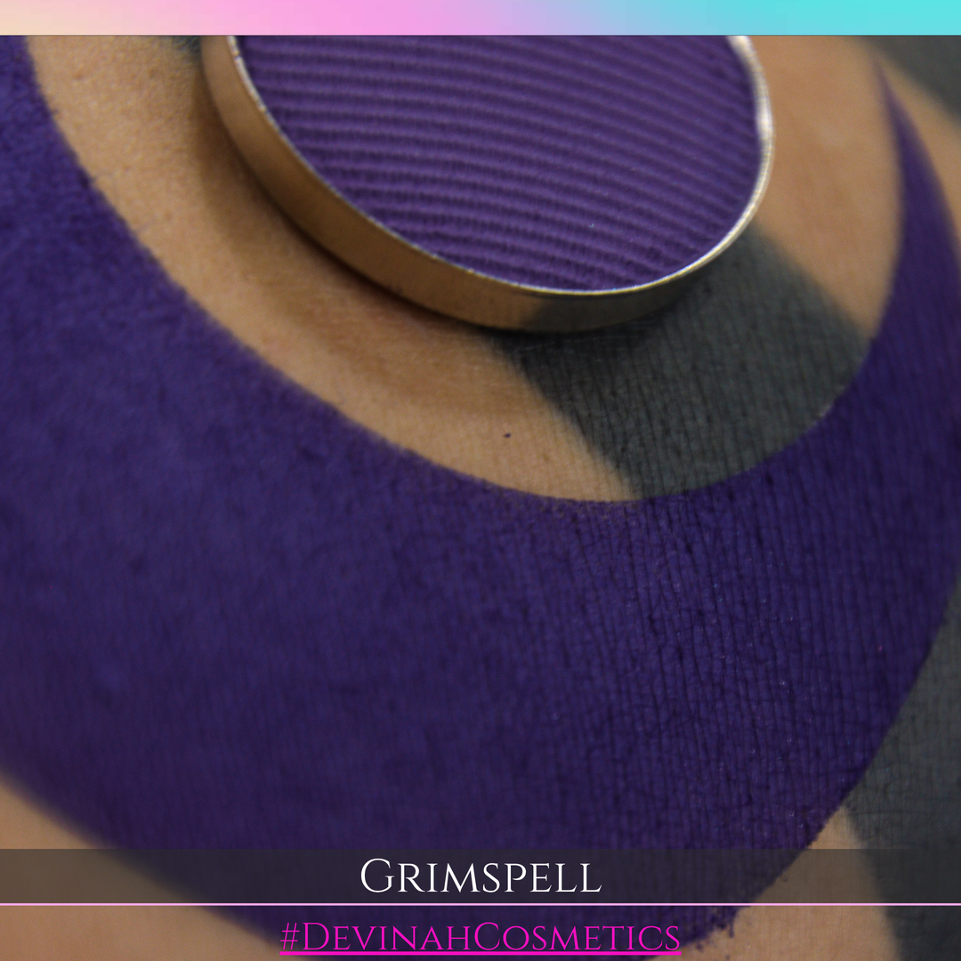 A close-up of a textured purple eyeshadow pan resting on a person's skin, with a matching purple eyeshadow applied in a large curved shape. The text 'GRIMSPELL' and '#DEVINAHCOSMETICS' are displayed at the bottom.