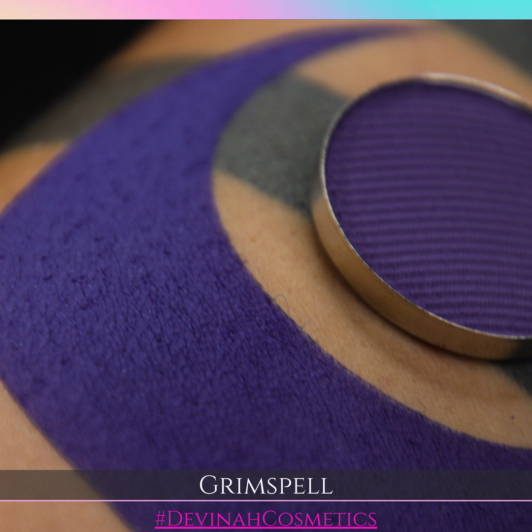 A close-up of a textured purple eyeshadow pan resting on a patterned surface with the text 'GRIMSPELL' and '#DEVINAHCOSMETICS' at the bottom.