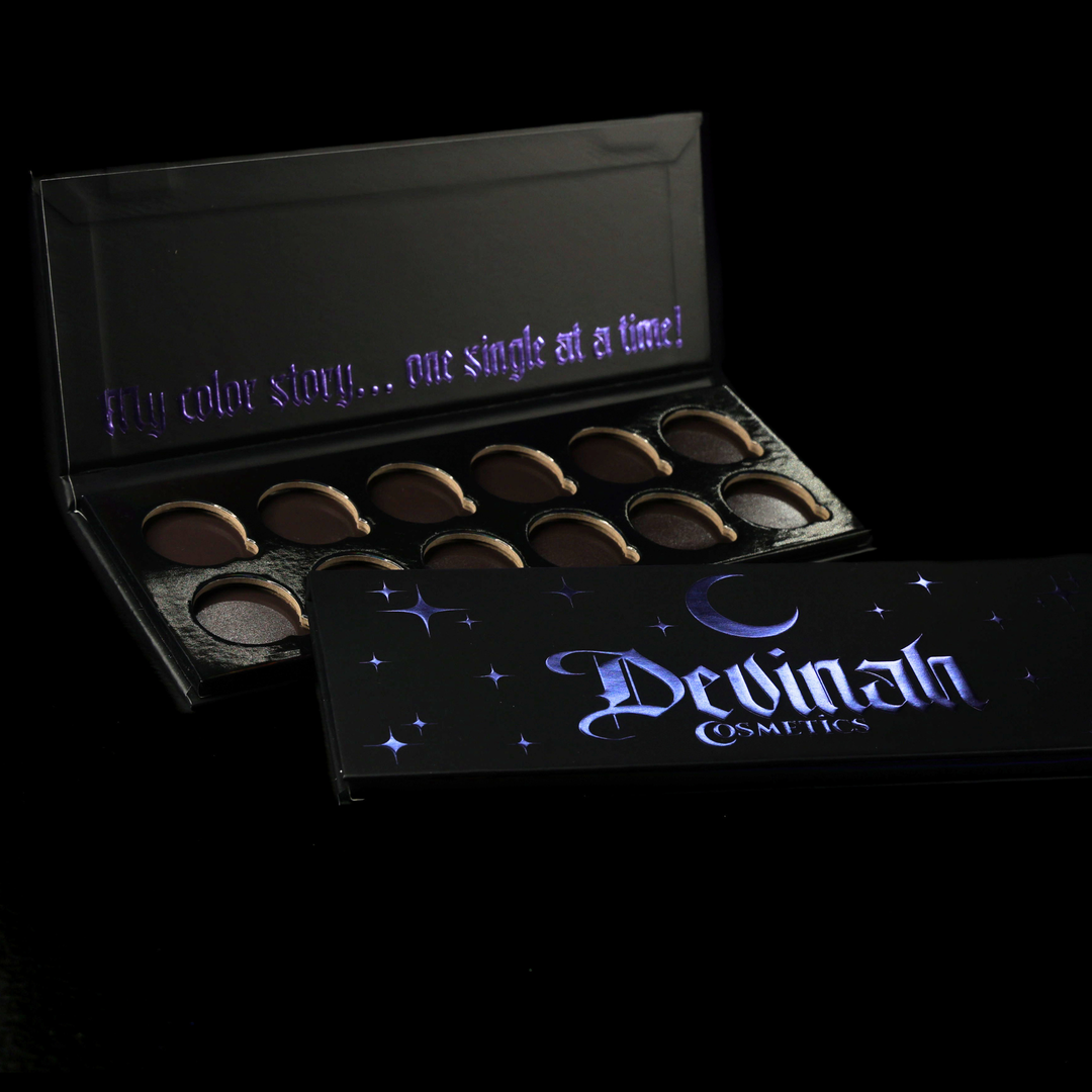 Two black makeup palettes from Devinah Cosmetics on a black background, one open showing circular pans and the other closed with glowing purple gothic lettering and stars with a crescent moon.