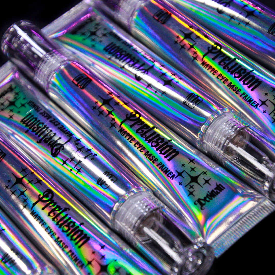 Several small iridescent cosmetic tubes labeled 'Prelusion' and 'Matte Eye Base Primer' arranged diagonally on a black background.