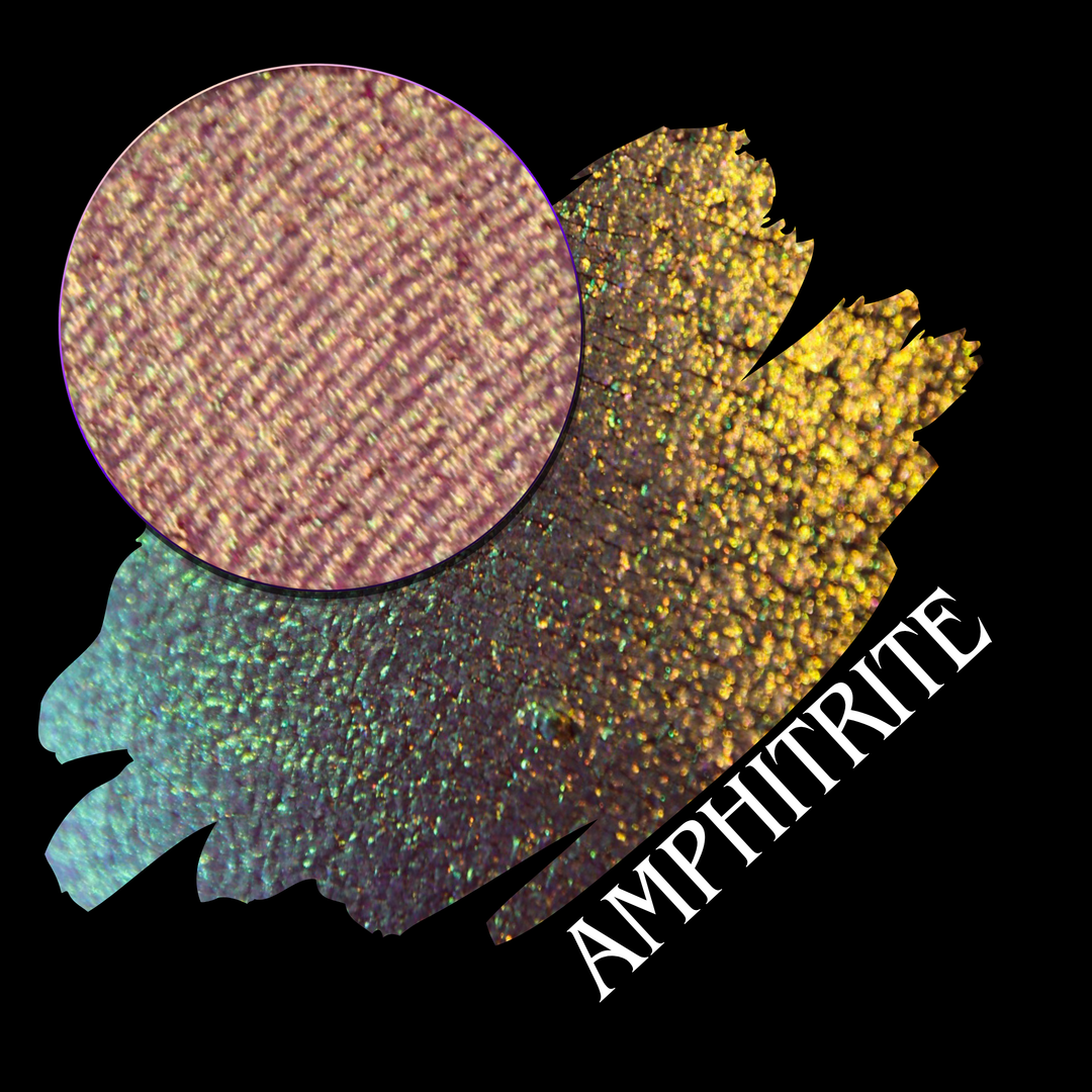 A round eyeshadow pan labeled 'AMPHITRITE' made by Devinah Cosmetics, placed over a large crescent moon swatch of the same shimmering shifty eyeshadow on skin. The eyeshadow has a shift between colors green, gold, purple, blue.