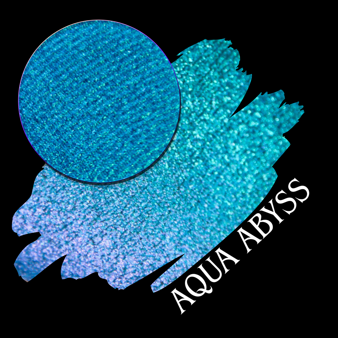 A round eyeshadow pan labeled 'AQUA ABYSS' made by Devinah Cosmetics, placed over a large crescent moon swatch of the same shimmering shifty eyeshadow on skin. The eyeshadow has a duochrome multichrome shift between colors lime green, blue, teal, pink.