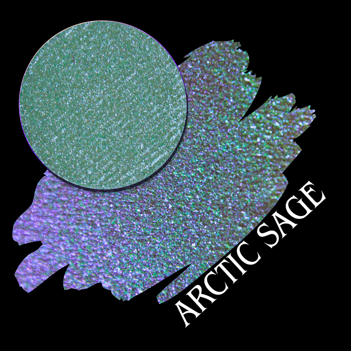 An eyeshadow swatch showing a shift in shimmer of a green-teal and purple-lavender blend, with a circular eyeshadow makeup pan and the text 'ARCTIC SAGE' on a black background handmade from indie brand Devinah Cosmetics.