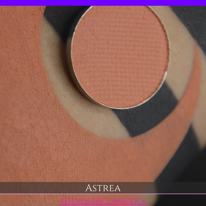 A close-up of a person's arm with a large peach-toned makeup swatch and a matching round eyeshadow makeup pan labeled ASTREA, with the text #DEVINAHCOSMETICS at the bottom.
