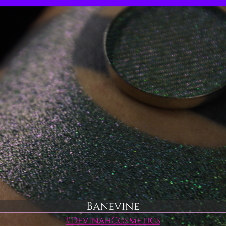 A close-up of a person's arm with a large crescent-shaped swatch of shimmering green eyeshadow, featuring a small round pan of the same green makeup placed on top. The text 'BANEVINE' and '#DEVINAHCOSMETICS' appear at the bottom.