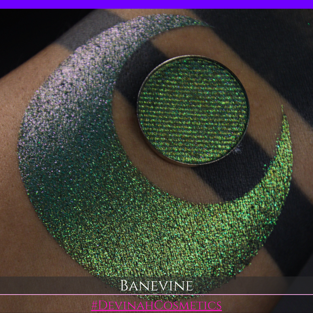 A close-up of a person's arm with a large crescent-shaped swatch of shimmering green eyeshadow, featuring a small round pan of the same green makeup placed on top. The text 'BANEVINE' and '#DEVINAHCOSMETICS' appear at the bottom.