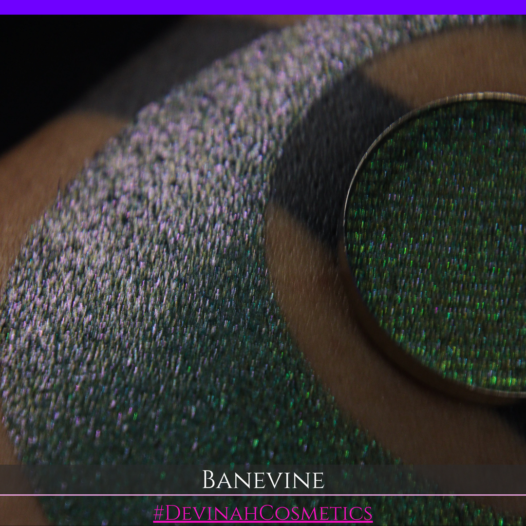 A close-up of a person's arm with a large crescent-shaped swatch of shimmering green eyeshadow, featuring a small round pan of the same green makeup placed on top. The text 'BANEVINE' and '#DEVINAHCOSMETICS' appear at the bottom.