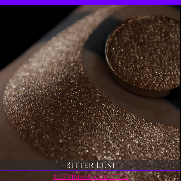 A round eyeshadow pan labeled 'BITTER LUST' made by Devinah Cosmetics, placed over a large crescent moon swatch of the same shimmering shifty eyeshadow on skin. The eyeshadow has shimmer sparkle colors brown, tan, beige, neutral.