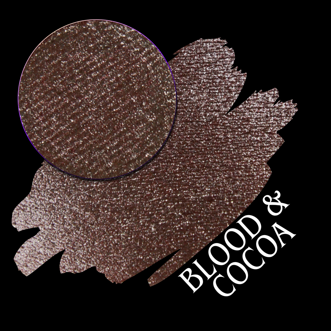 A round eyeshadow pan labeled 'BLOOD AND COCOA' made by Devinah Cosmetics, placed over a large crescent moon swatch of the same shimmering shifty eyeshadow on skin. The eyeshadow has shimmery sparkle of red infused chocolate shimmer.