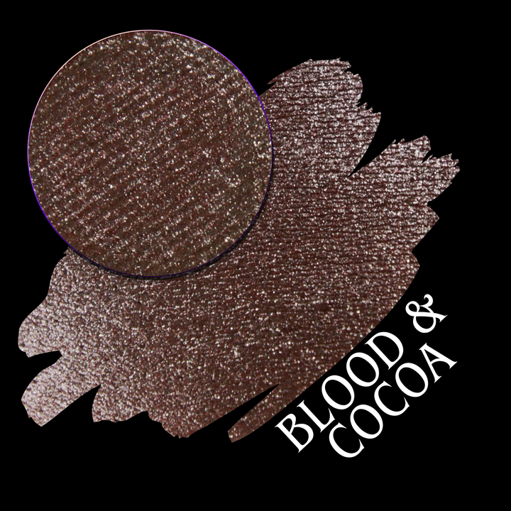 A round eyeshadow pan labeled 'BLOOD AND COCOA' made by Devinah Cosmetics, placed over a large crescent moon swatch of the same shimmering shifty eyeshadow on skin. The eyeshadow has shimmery sparkle of red infused chocolate shimmer.