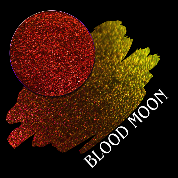 A textured color swatch showing a glittery red circular eyeshadow makeup pan and a larger irregular swatch blending red, orange, and yellow tones, with the text 'BLOOD MOON' on a black background.
