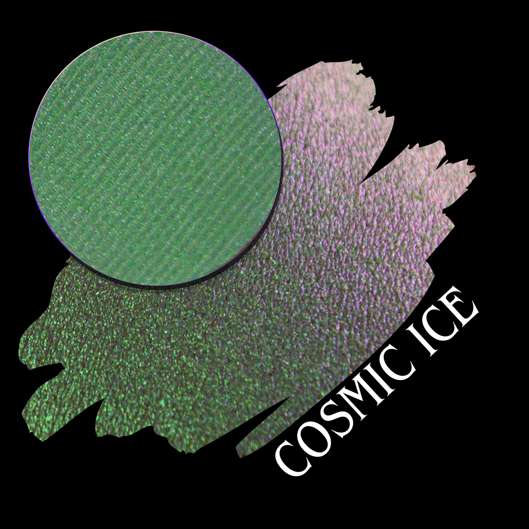 A circular eyeshadow pan, layered over an eyeshadow swatch that shifts from green to iridescent lavender-pink. The text 'COSMIC ICE' appears diagonally over the swatch on a black background made by Devinah Cosmetics.