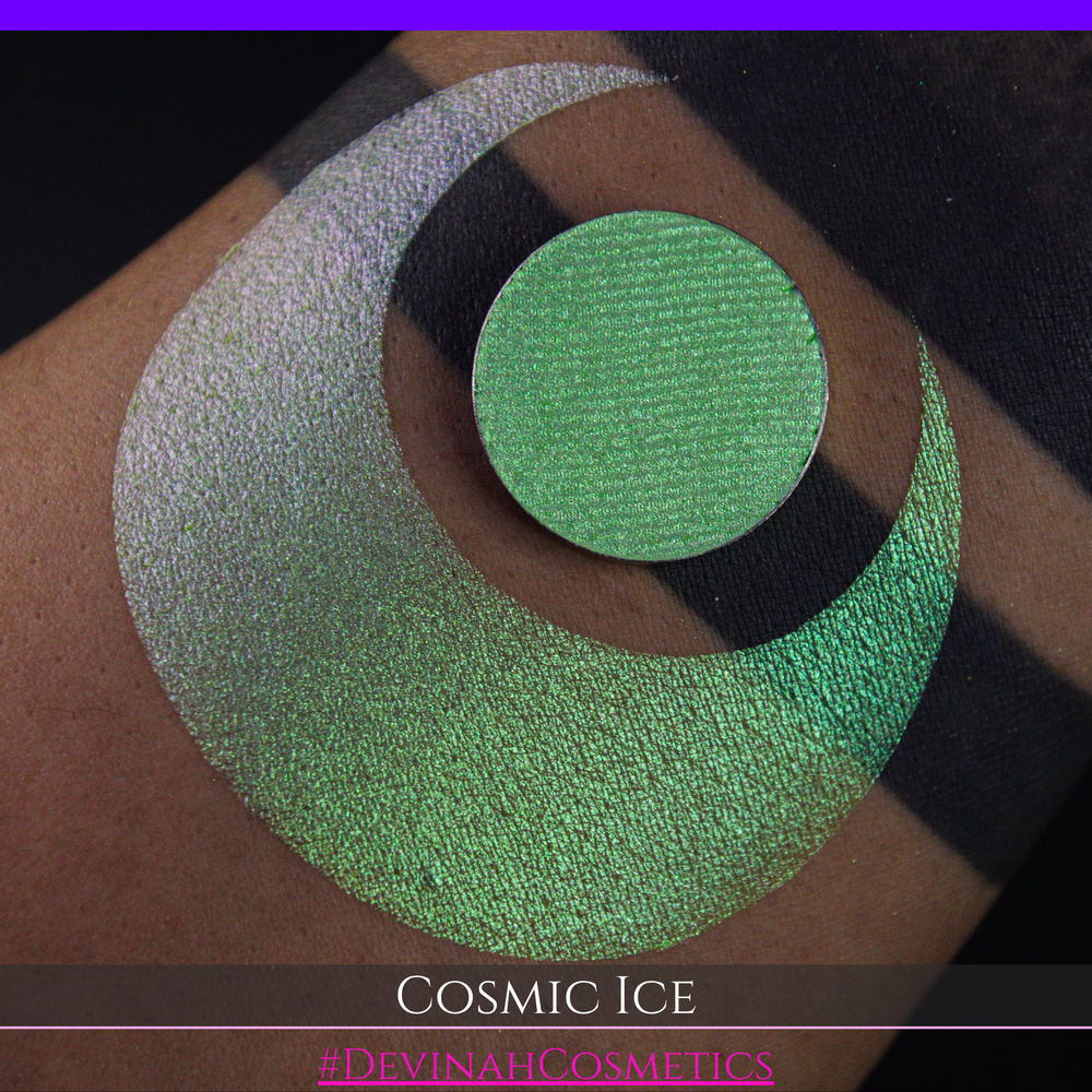 A close-up of a person's arm showing a shimmery green eyeshadow in a circular pan, placed over a larger swatch. Text at the bottom reads 'Cosmic Ice' and '#DevinahCosmetics'.