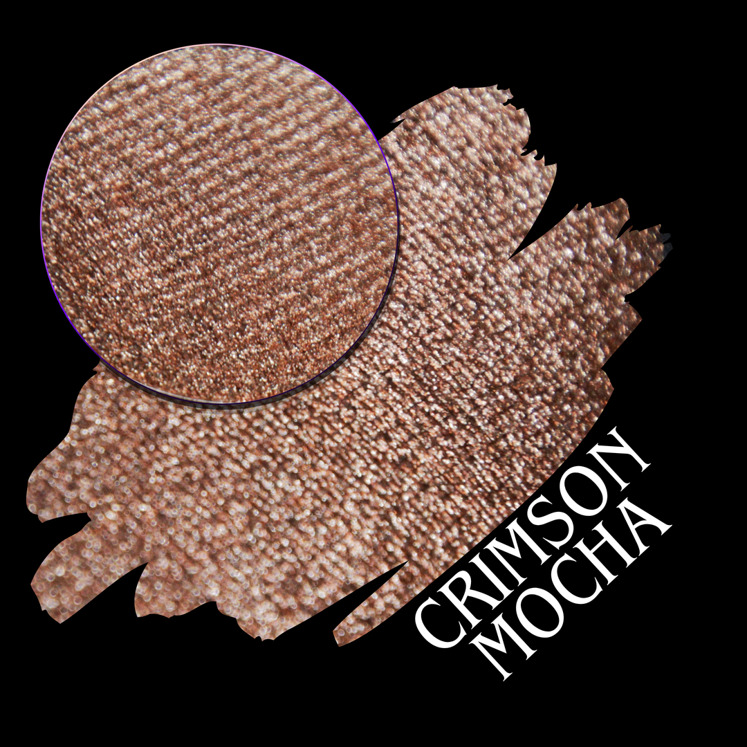A round eyeshadow pan labeled 'CRIMSON MOCHA' made by Devinah Cosmetics, placed over a large crescent moon swatch of the same shimmering shifty eyeshadow on skin. The eyeshadow has colors of sparkly red and brown shimmer.