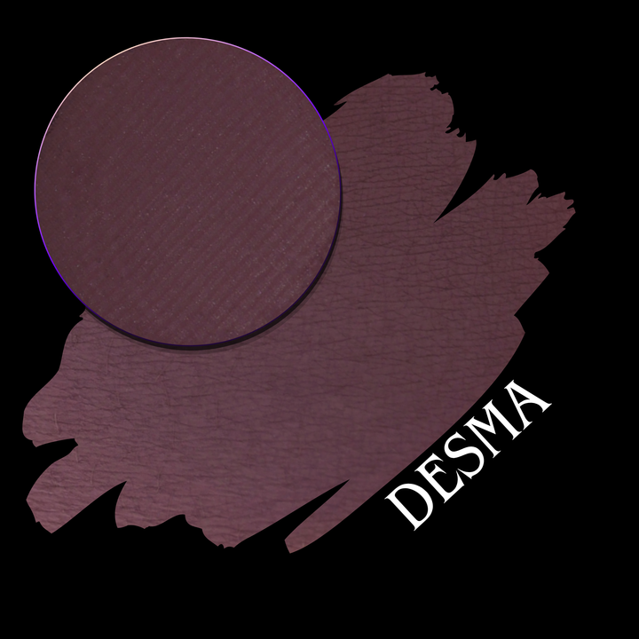 A makeup swatch showing a deep plum-purple color, with a circular makeup eyeshadow pan on a black background. The text 'DESMA' is written in white at the bottom right.