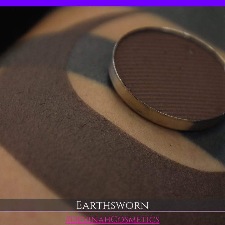 A makeup swatch showing a brown eyeshadow with a circular eyeshadow makeup pan, labeled 'EARTHSWORN' on a black background.