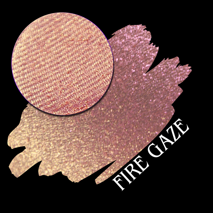 A makeup color swatch showing a shimmering pink-rose eyeshadow with a circular eyeshadow pan and the text 'FIRE GAZE' on a black background made by Devinah Cosmetics.