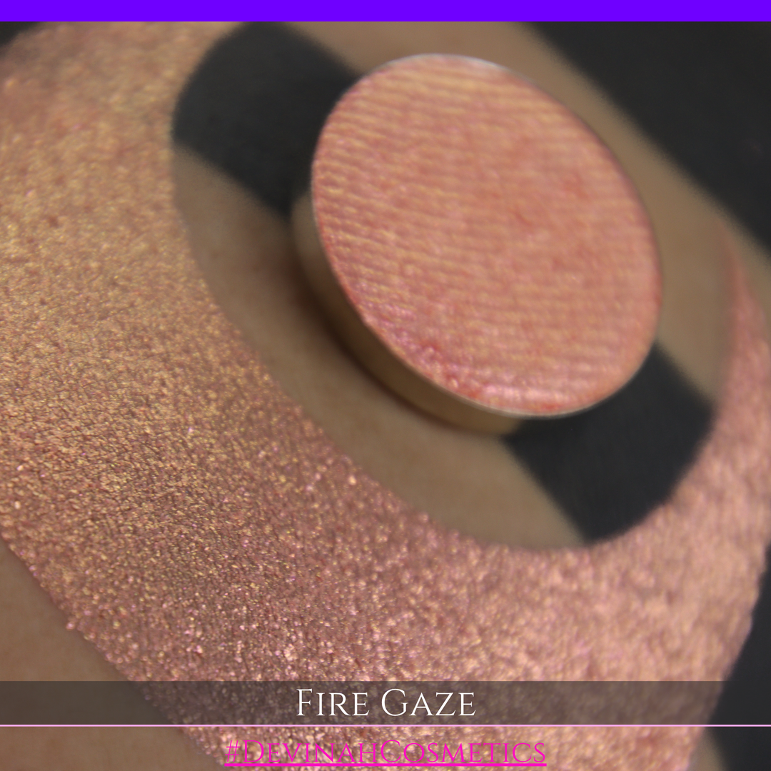 A makeup color swatch showing a shimmering pink-rose eyeshadow with a circular eyeshadow pan and the text 'FIRE GAZE' on a black background made by Devinah Cosmetics.