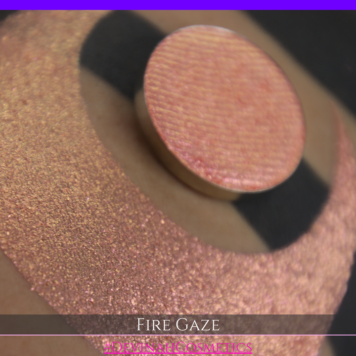 A makeup color swatch showing a shimmering pink-rose eyeshadow with a circular eyeshadow pan and the text 'FIRE GAZE' on a black background made by Devinah Cosmetics.