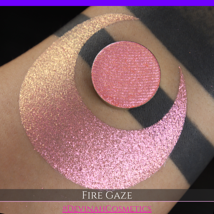 A makeup color swatch showing a shimmering pink-rose eyeshadow with a circular eyeshadow pan and the text 'FIRE GAZE' on a black background made by Devinah Cosmetics.