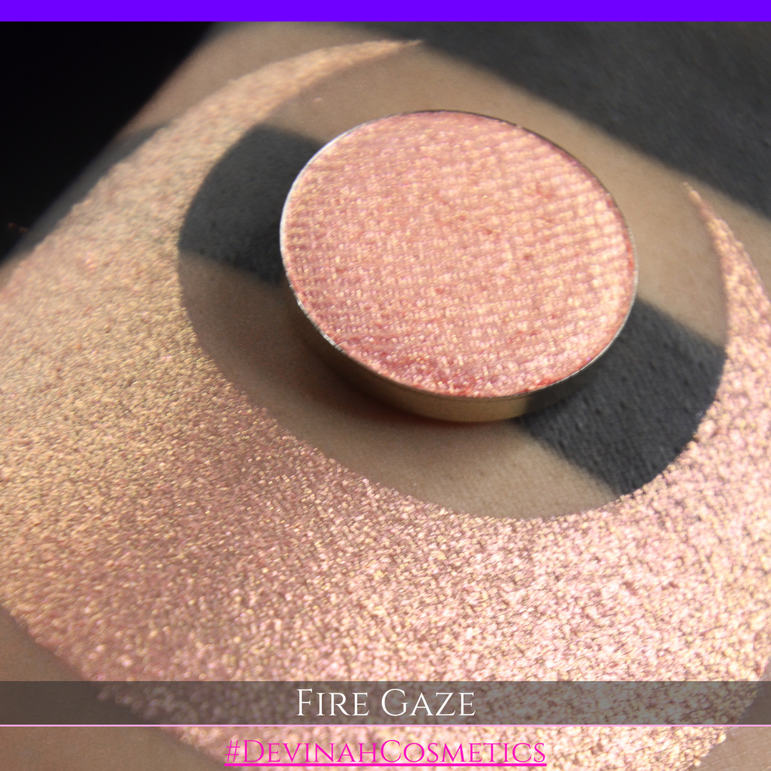 A makeup color swatch showing a shimmering pink-rose eyeshadow with a circular eyeshadow pan and the text 'FIRE GAZE' on a black background made by Devinah Cosmetics.