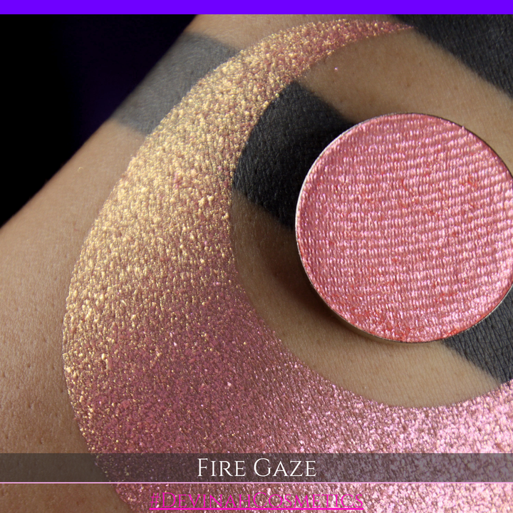 A makeup color swatch showing a shimmering pink-rose eyeshadow with a circular eyeshadow pan and the text 'FIRE GAZE' on a black background made by Devinah Cosmetics.