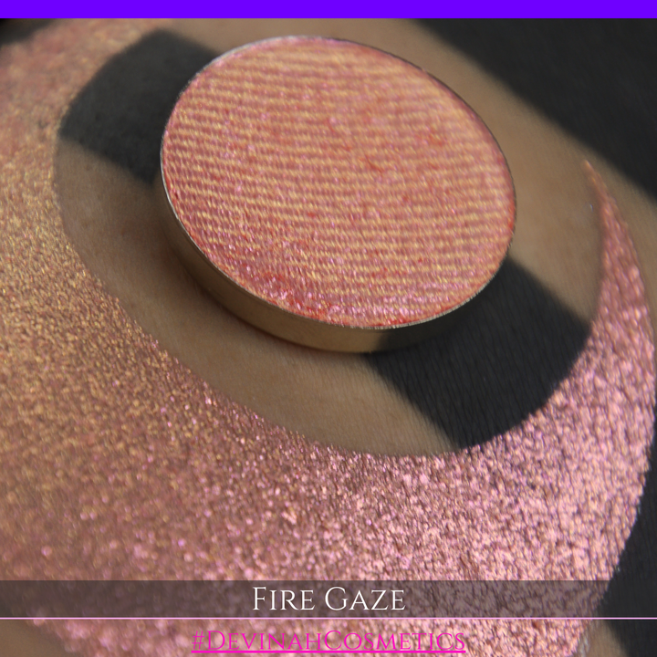 A makeup color swatch showing a shimmering pink-rose eyeshadow with a circular eyeshadow pan and the text 'FIRE GAZE' on a black background made by Devinah Cosmetics.