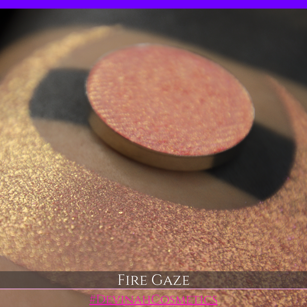 A makeup color swatch showing a shimmering pink-rose eyeshadow with a circular eyeshadow pan and the text 'FIRE GAZE' on a black background made by Devinah Cosmetics.
