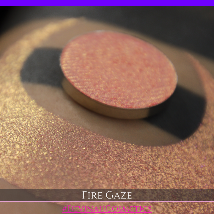 A makeup color swatch showing a shimmering pink-rose eyeshadow with a circular eyeshadow pan and the text 'FIRE GAZE' on a black background made by Devinah Cosmetics.