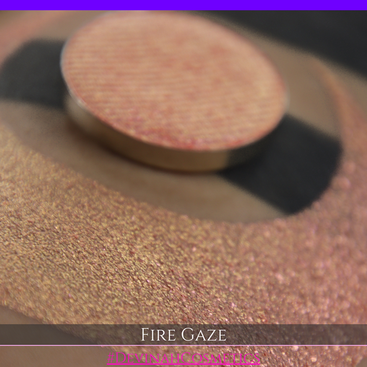 A makeup color swatch showing a shimmering pink-rose eyeshadow with a circular eyeshadow pan and the text 'FIRE GAZE' on a black background made by Devinah Cosmetics.