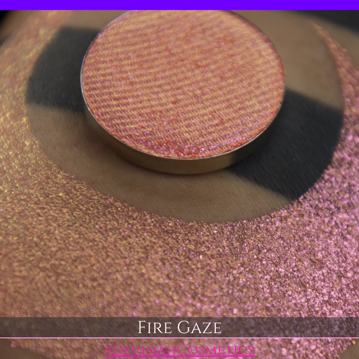 A makeup color swatch showing a shimmering pink-rose eyeshadow with a circular eyeshadow pan and the text 'FIRE GAZE' on a black background made by Devinah Cosmetics.