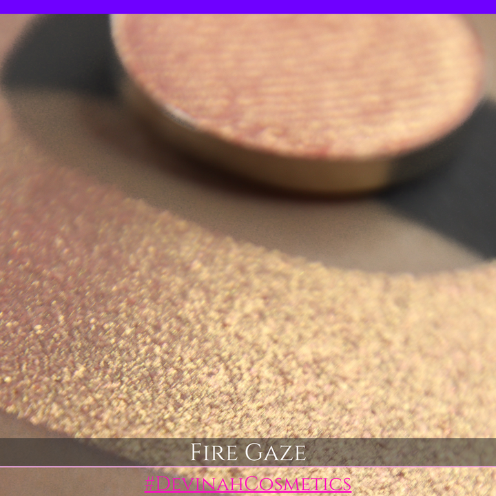 A makeup color swatch showing a shimmering pink-rose eyeshadow with a circular eyeshadow pan and the text 'FIRE GAZE' on a black background made by Devinah Cosmetics.