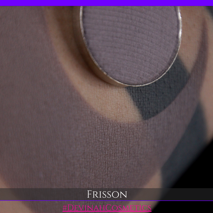 Close-up of a makeup palette showing a circular pan of dusty mauve-purple powder, with swatches of the shade applied on skin. The text 'FRISSON' and '#DEVINAH COSMETICS' are visible at the bottom.