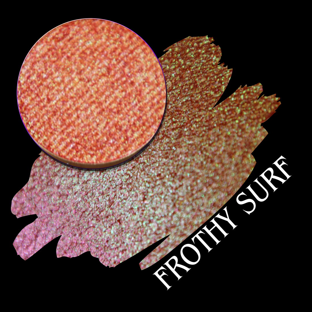 A round eyeshadow pan labeled 'FROTHY SURF' made by Devinah Cosmetics, placed over a large crescent moon swatch of the same shimmering shifty eyeshadow on skin. The eyeshadow has a duochrome multichrome shift between colors green, yellow, gold, orange, pink, red.