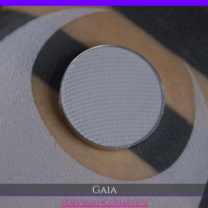 A circular makeup pan containing a light gray powder, resting on a textured surface with a black, beige, and white circular pattern. The text 'GAIA' is displayed at the bottom.