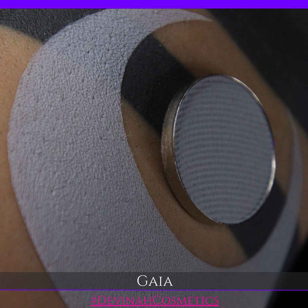 Close-up of a circular metallic device with a textured gray surface, mounted on a beige circular patch over skin. The image has a purple top border, a dark bottom banner with the text 'GAIA' and '#DEVINAHCOSMETICS', and a black background.