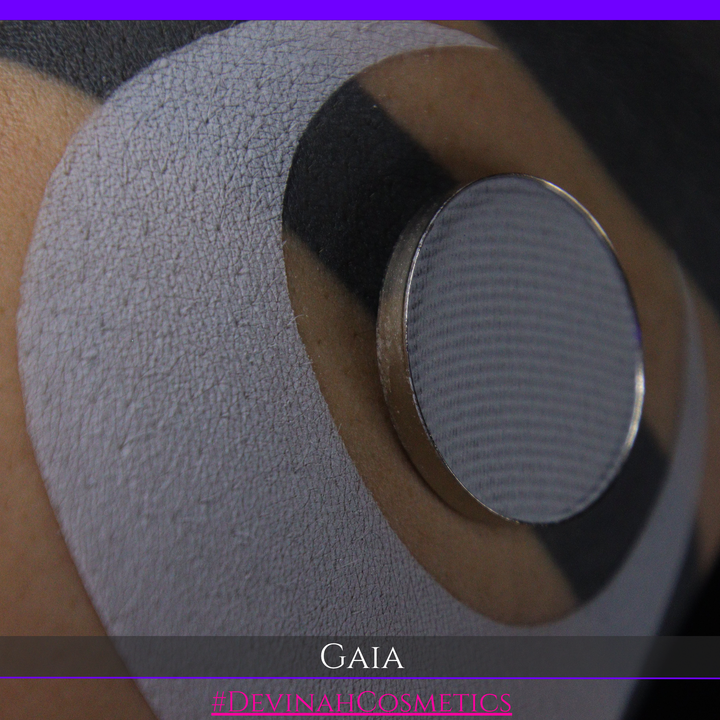 Close-up of a circular metallic device with a textured gray surface, mounted on a beige circular patch over skin. The image has a purple top border, a dark bottom banner with the text 'GAIA' and '#DEVINAHCOSMETICS', and a black background.