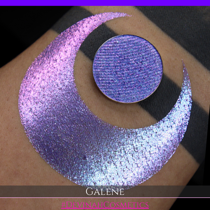 A round eyeshadow pan labeled 'GALENE' made by Devinah Cosmetics, placed over a large crescent moon swatch of the same shimmering shifty eyeshadow on skin. The duochorme multichrome eyeshadow has a shift between colors pink, purple, blue.