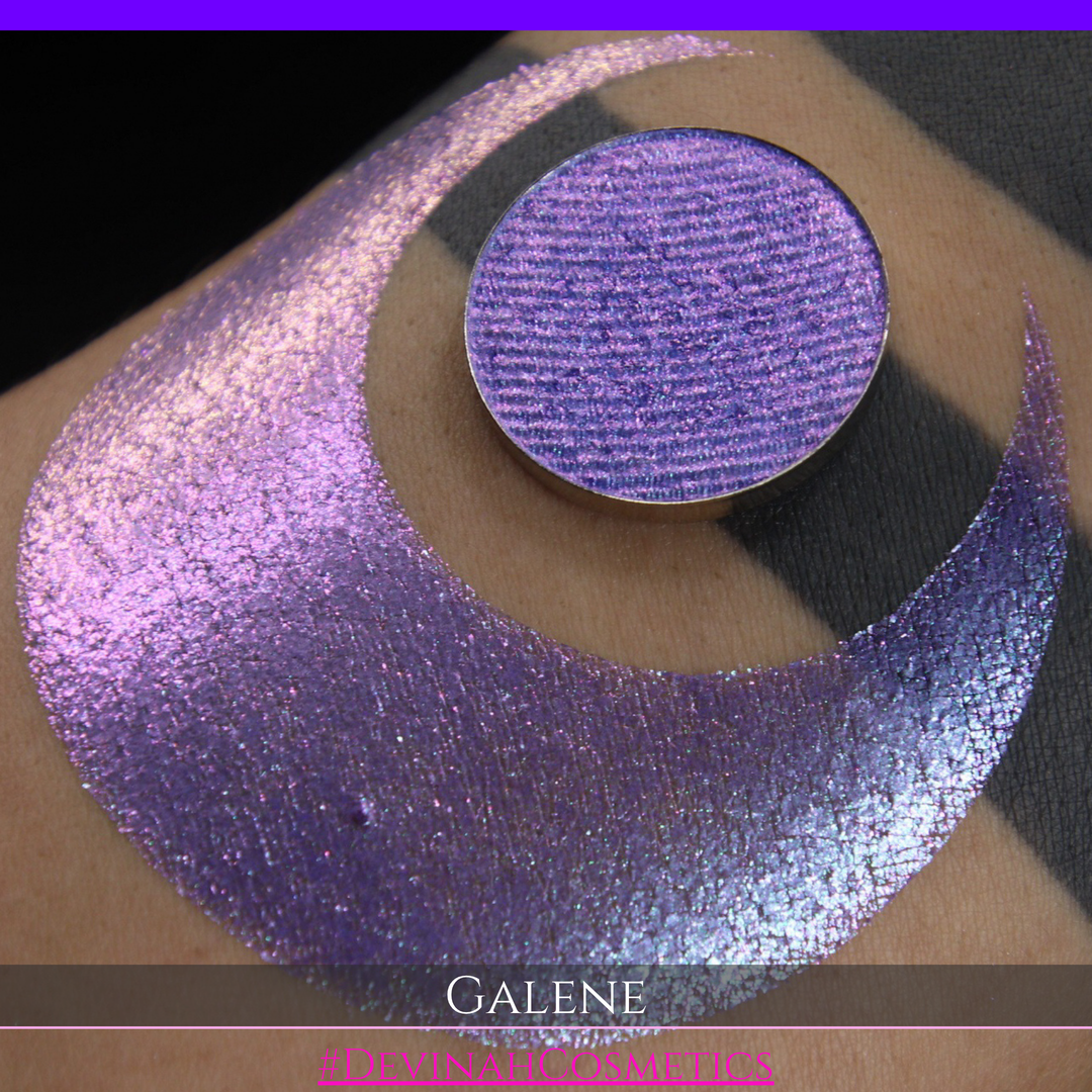 A round eyeshadow pan labeled 'GALENE' made by Devinah Cosmetics, placed over a large crescent moon swatch of the same shimmering shifty eyeshadow on skin. The duochorme multichrome eyeshadow has a shift between colors pink, purple, blue.