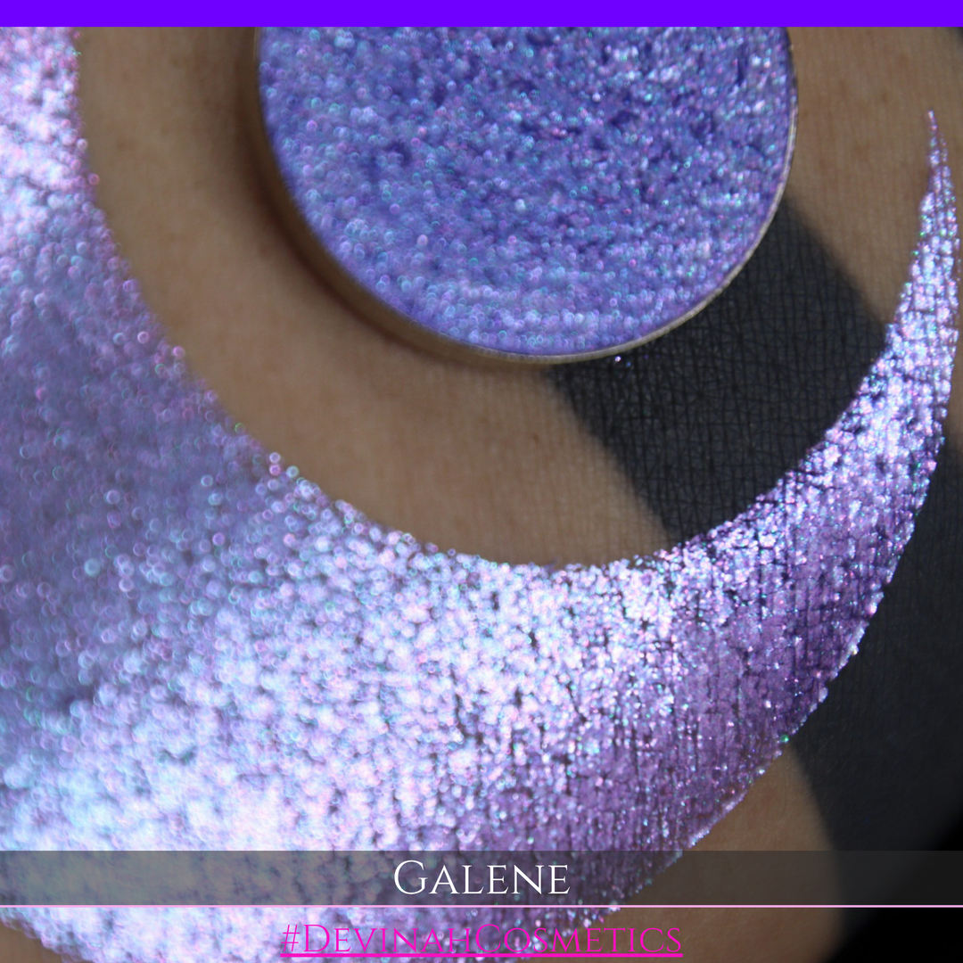 A round eyeshadow pan labeled 'GALENE' made by Devinah Cosmetics, placed over a large crescent moon swatch of the same shimmering shifty eyeshadow on skin. The duochorme multichrome eyeshadow has a shift between colors pink, purple, blue.