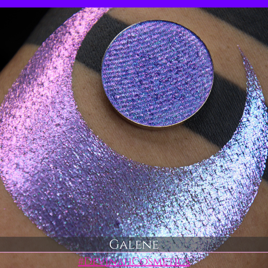 A round eyeshadow pan labeled 'GALENE' made by Devinah Cosmetics, placed over a large crescent moon swatch of the same shimmering shifty eyeshadow on skin. The duochorme multichrome eyeshadow has a shift between colors pink, purple, blue.
