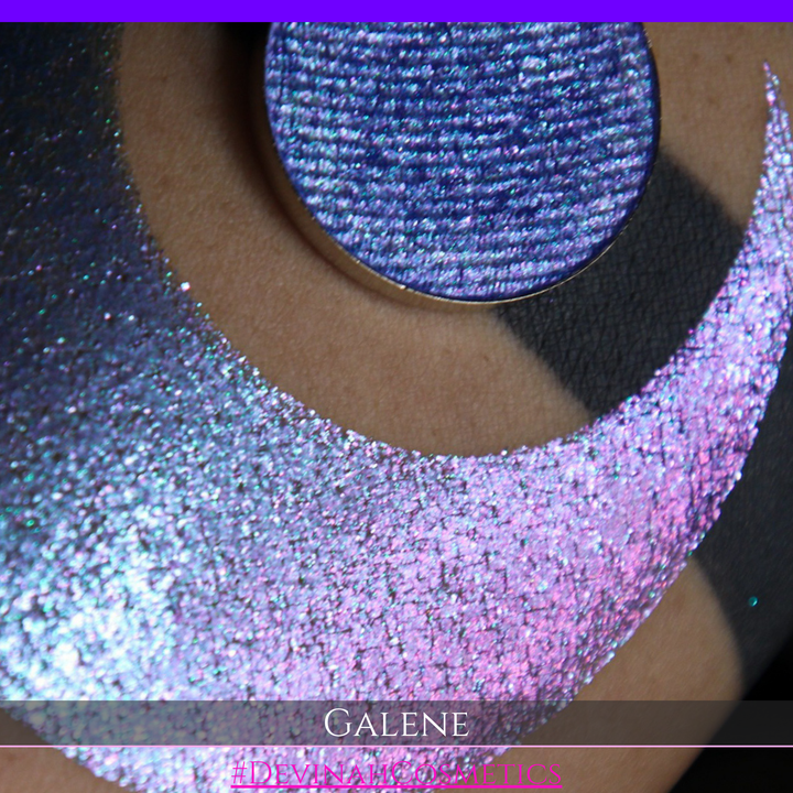 A round eyeshadow pan labeled 'GALENE' made by Devinah Cosmetics, placed over a large crescent moon swatch of the same shimmering shifty eyeshadow on skin. The duochorme multichrome eyeshadow has a shift between colors pink, purple, blue.
