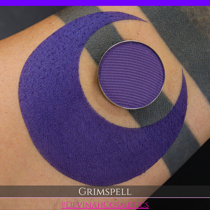 A close-up of a purple matte eyeshadow swatch and the eyeshadow pan. The text 'GRIMSPELL' and '#DEVINAHCosmetics' are displayed at the bottom.