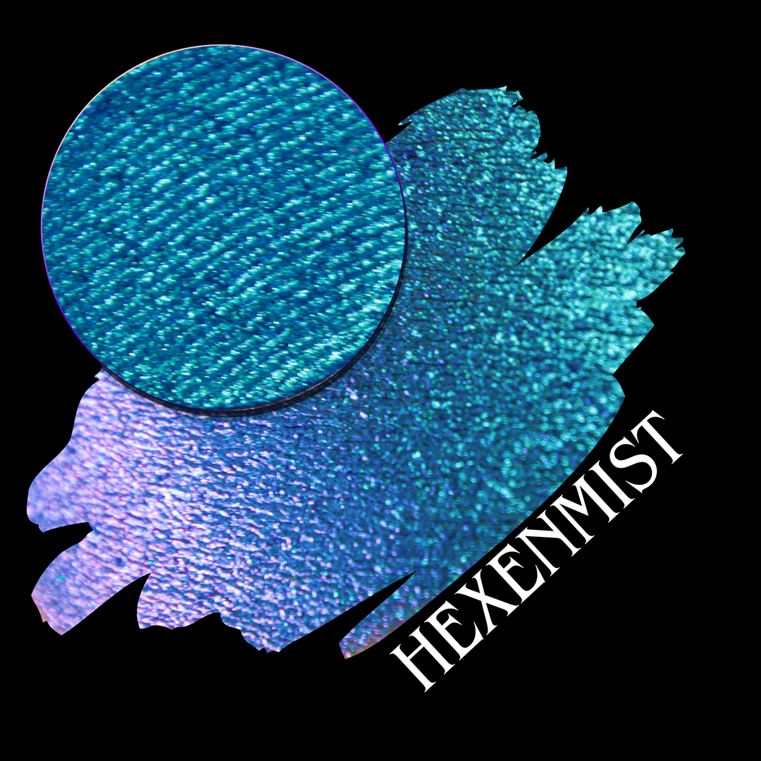A swatch showing a shimmering eyeshadow that shifts from cyan-blue to light purple, with a circular eyeshadow pan and the word 'HEXENMIST' written diagonally on a black background made by Devinah Cosmetics.