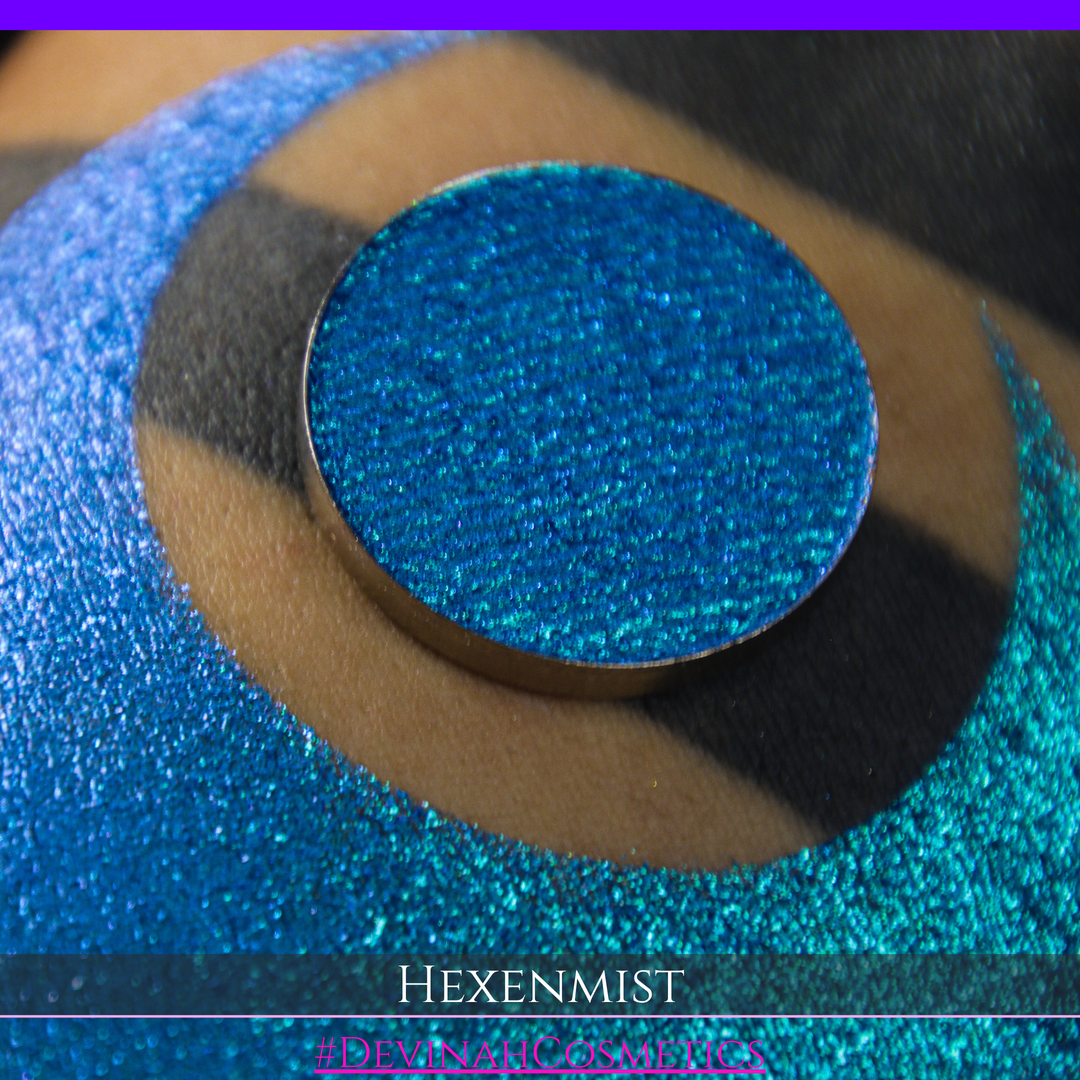 A close-up of a large crescent swatch of shimmering eyeshadow makeup in bright teal, aqua, and purple tones. The text 'HEXENMIST' and '#DEVINAHCOSMETICS' appear at the bottom.