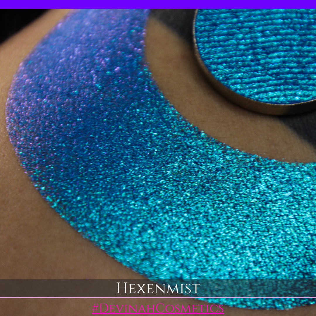 A close-up of a large crescent swatch of shimmering eyeshadow makeup in bright teal, aqua, and purple tones. The text 'HEXENMIST' and '#DEVINAHCOSMETICS' appear at the bottom.
