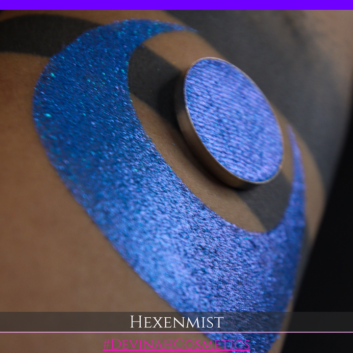A close-up of a large crescent swatch of shimmering eyeshadow makeup in bright teal, aqua, and purple tones. The text 'HEXENMIST' and '#DEVINAHCOSMETICS' appear at the bottom.