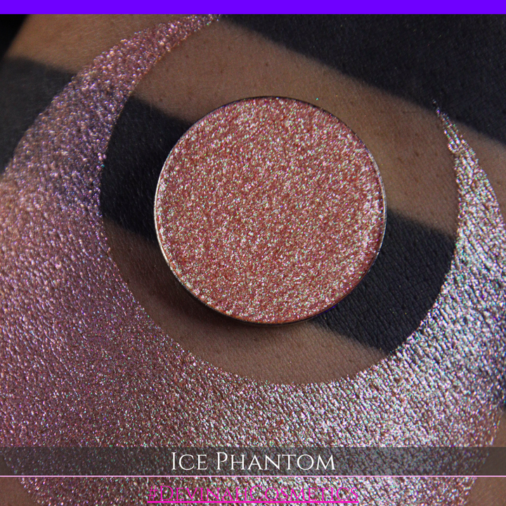 A circular makeup eyeshadow pan of a shimmery rose gold peachy coral eyeshadow labeled 'ICE PHANTOM' by Devinah Cosmetics, shown next to a large swatch on skin.