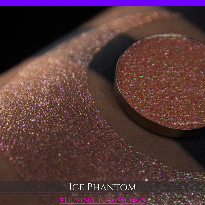 A circular makeup eyeshadow pan of a shimmery rose gold peachy coral eyeshadow labeled 'ICE PHANTOM' by Devinah Cosmetics, shown next to a large swatch on skin.