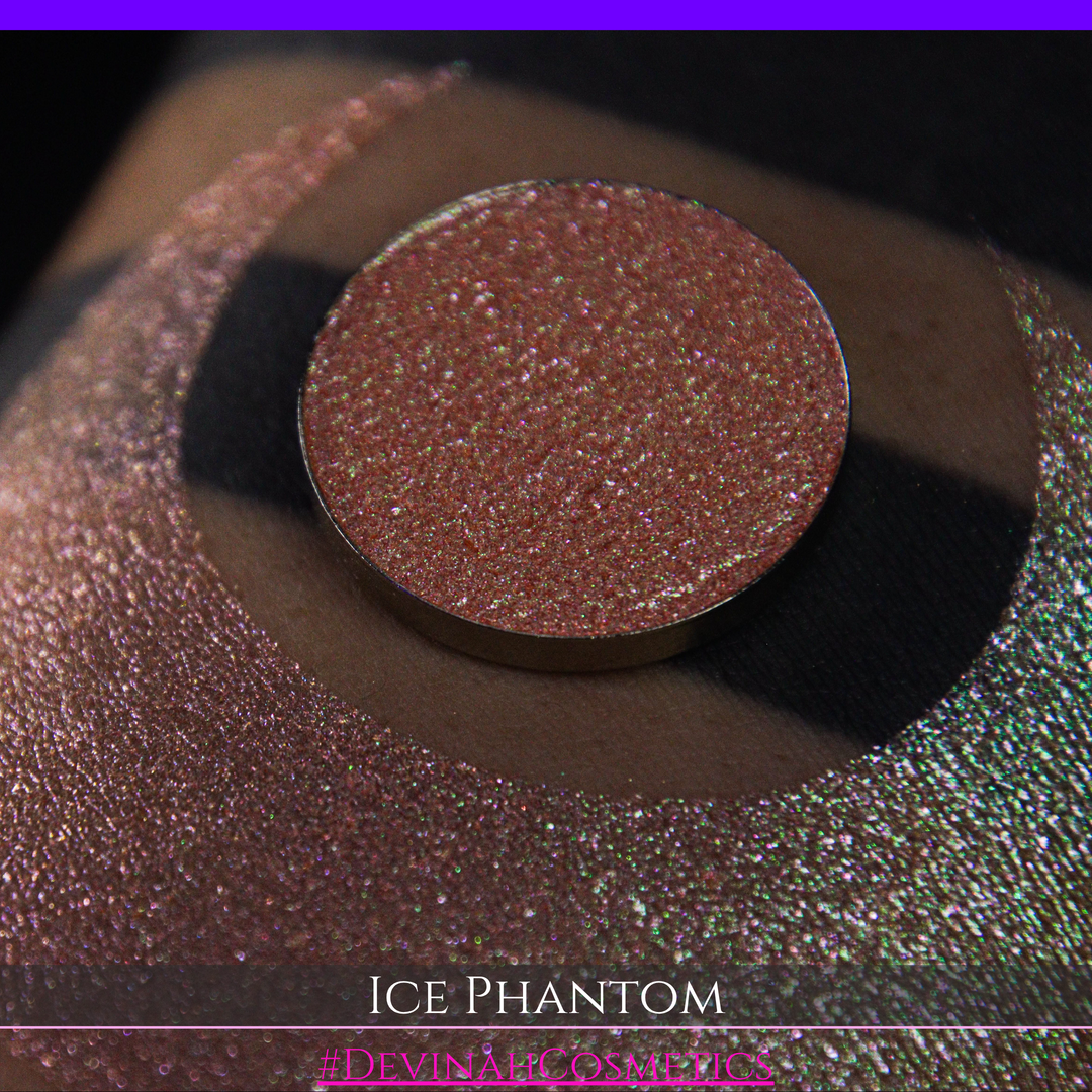 A circular makeup eyeshadow pan of a shimmery rose gold peachy coral eyeshadow labeled 'ICE PHANTOM' by Devinah Cosmetics, shown next to a large swatch on skin.